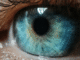 Close-up of a human blue eye showing detailed iris patterns with shades of blue, green, and hints of gold around the pupil, along with visible eyelashes.