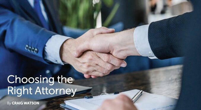 Two business professionals in suits shake hands across a polished desk, symbolizing trust and partnership during a legal consultation. A clipboard with papers and a pen rests in the foreground.