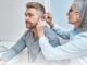 A healthcare professional examines a middle-aged man’s ear during a hearing check-up in a clinical setting.