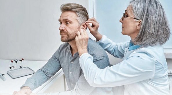 A healthcare professional examines a middle-aged man’s ear during a hearing check-up in a clinical setting.