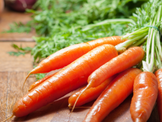 Bunch of fresh carrots with green tops on a wooden cutting board, illustrating foods that support eye health