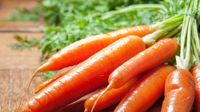 Bunch of fresh carrots with green tops on a wooden cutting board, illustrating foods that support eye health